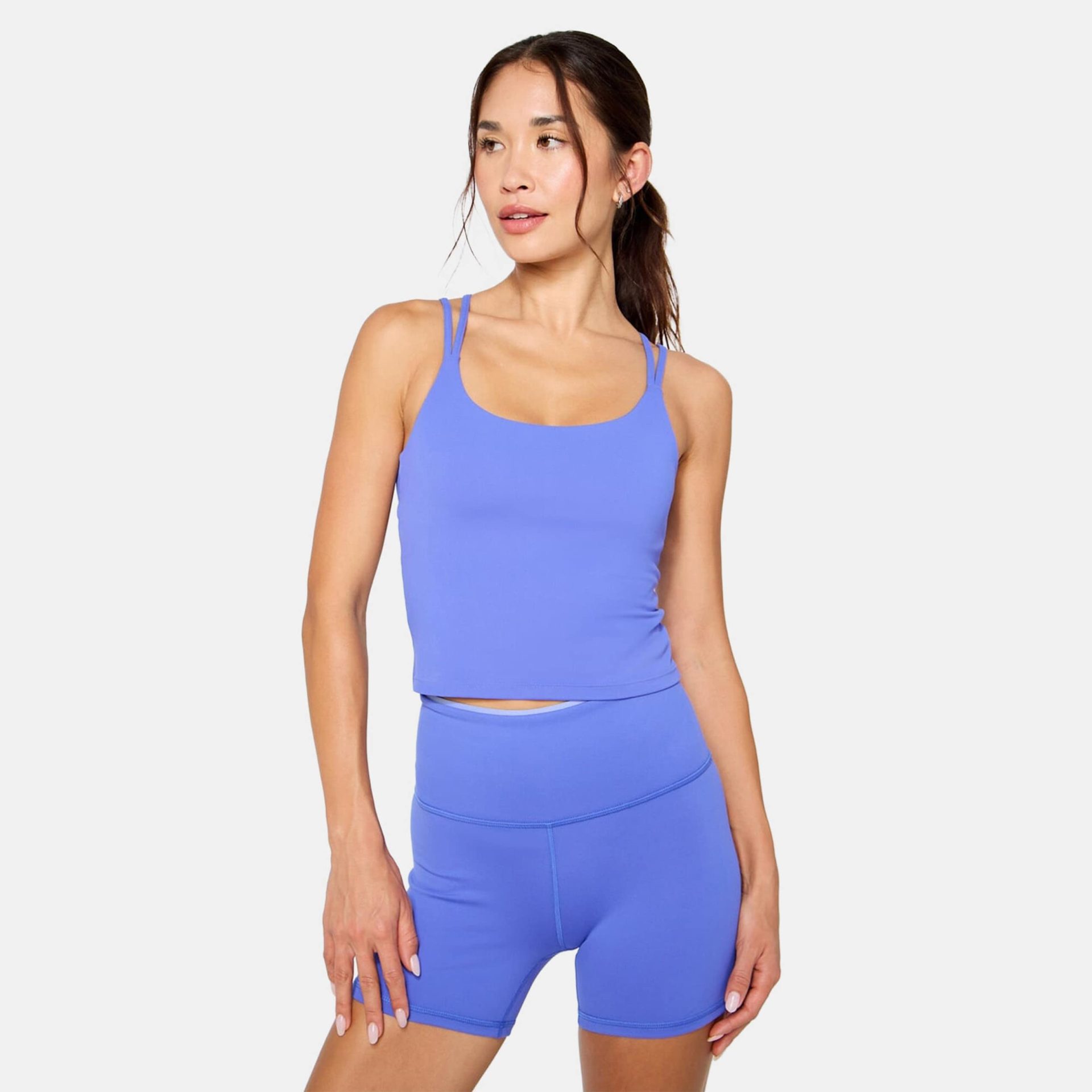 A woman with dark hair tied back wears a bright blue athletic tank top with double straps and matching high-waisted biker shorts.