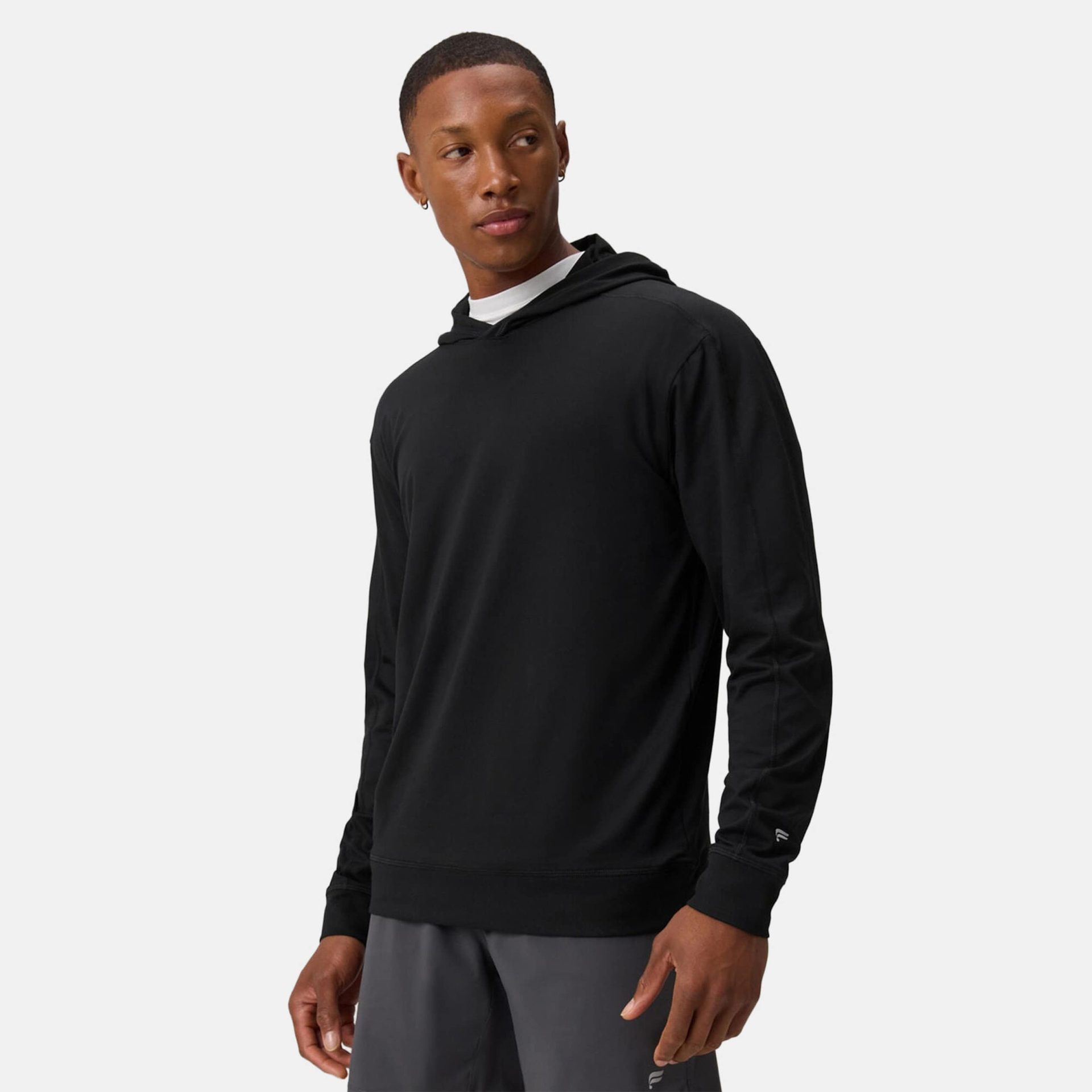A man wearing a black long-sleeve athletic hoodie over a white undershirt, paired with grey shorts.